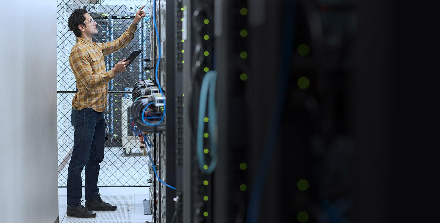 Man wearing glasses and a plaid shirt holding a tablet in a server room